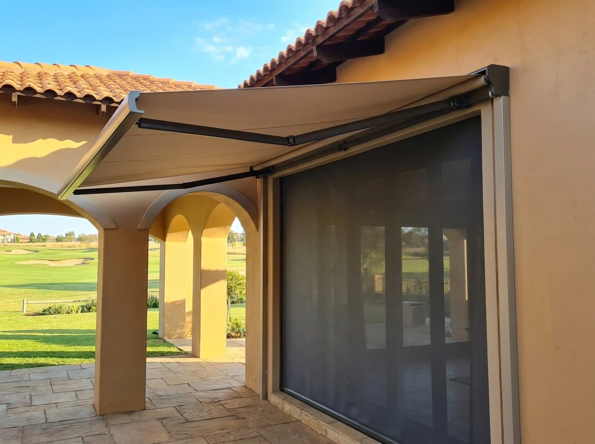 Folding-arm awning extended on hinged arms over a paved patio at a Tuscan-style estate home overlooking a golf green, with a flat mesh zip screen lowered in vertical side channels across the adjacent opening