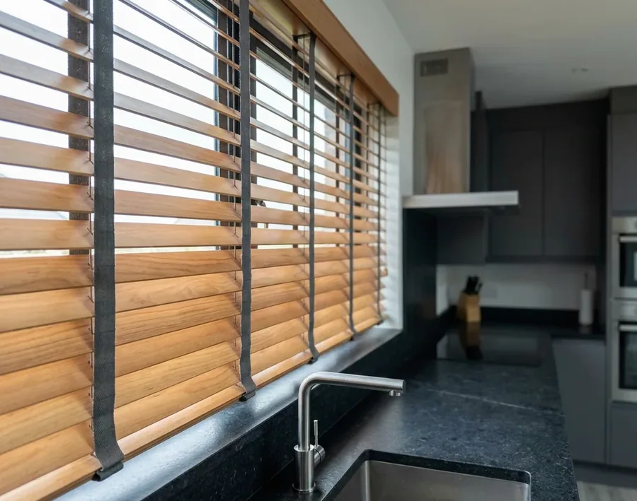 Timber venetian blind with horizontal wooden slats and ladder tapes tilted open above a kitchen counter